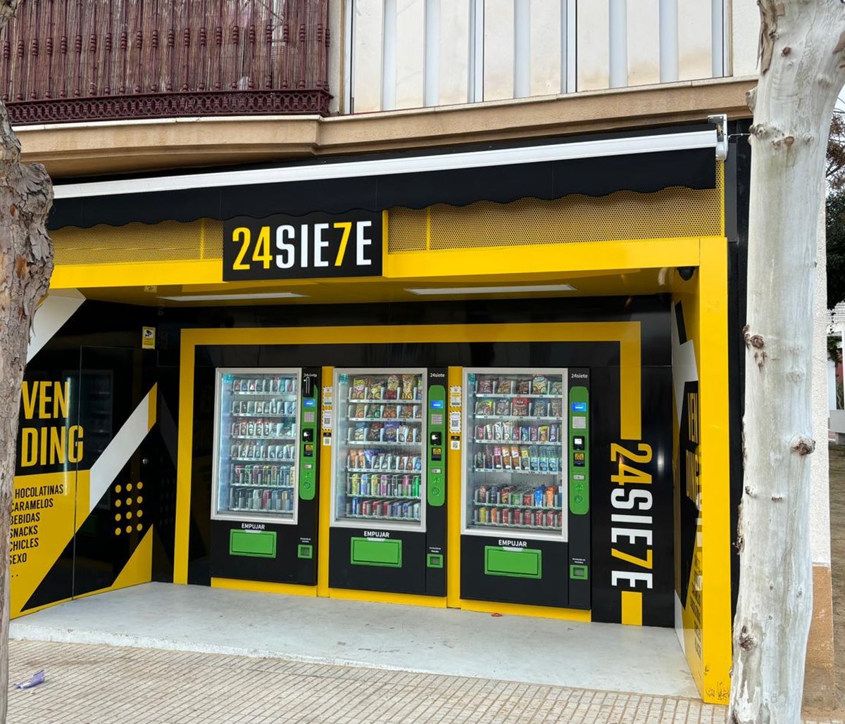 Fachada amarilla y negra de 24SIE7E con tres máquinas de bebidas y snacks